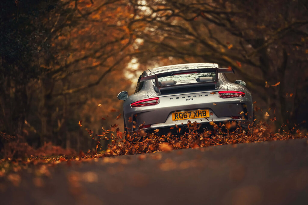 Porsche car speeding on autumn forest road with colorful leaves in 4K Ultra HD wallpaper background