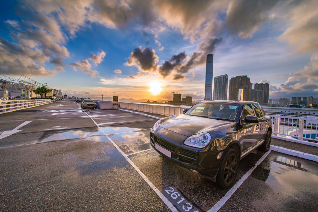 Sleek Porsche supercar on rooftop parking at sunset with city skyline and reflective puddles Wallpaper
