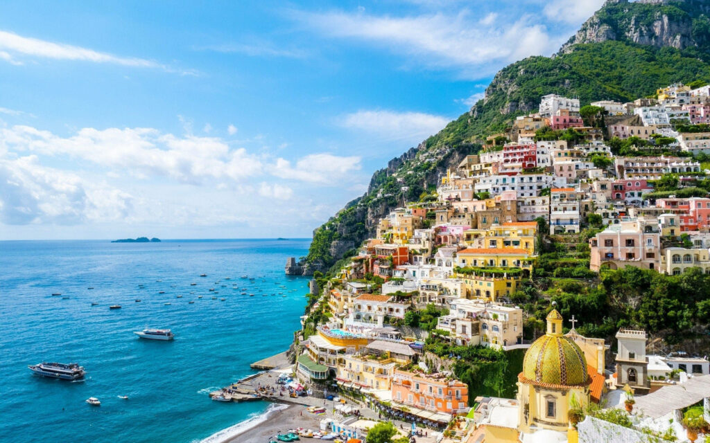 Morning view of colorful cliffside houses and boats on vibrant blue waters in Positano Italy Wallpaper