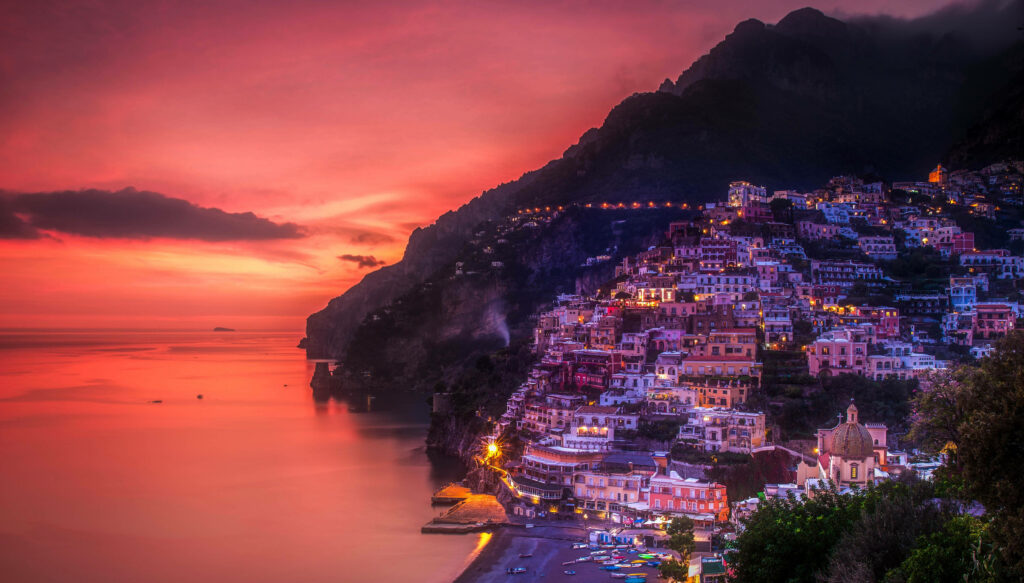 Positano sunset with colorful cliffside houses and vibrant pink purple sky over calm sea wallpaper