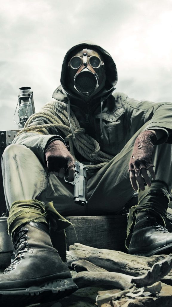 Post-apocalyptic survivor in gas mask and hooded gear holding pistol amid debris at dusk Wallpaper
