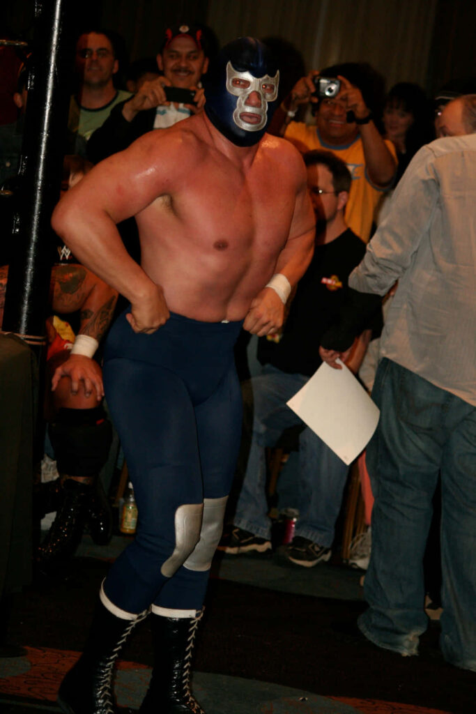 Muscular luchador in blue mask and tights at wrestling event with cheering fans background wallpaper