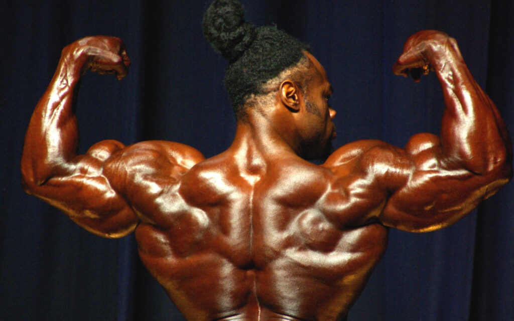 Bodybuilder flexing sculpted back and arm muscles on stage with wallpaper background