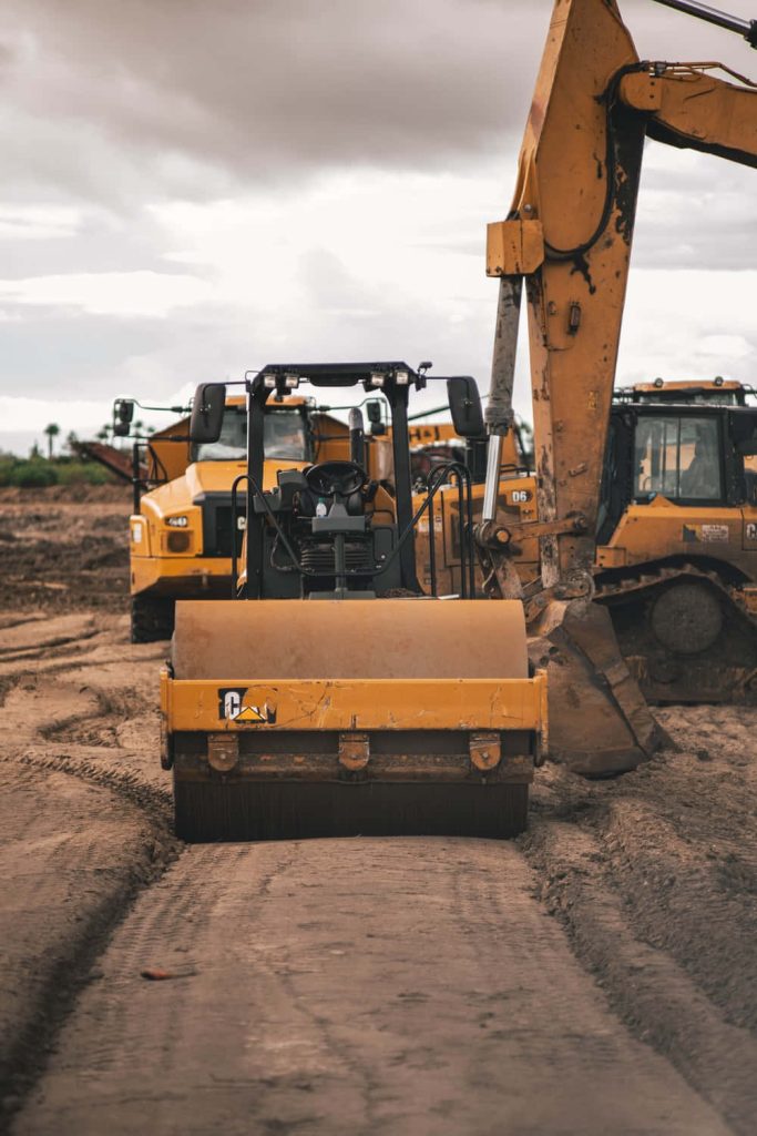 Caterpillar soil compactor and excavator on muddy road heavy machinery construction site background Wallpaper