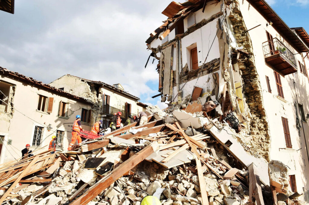 Earthquake aftermath with rescue workers amid rubble and collapsed buildings in muted tones Wallpaper