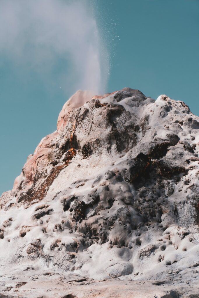 Powerful geyser erupting on rugged mountain with icy textures and clear blue sky wallpaper