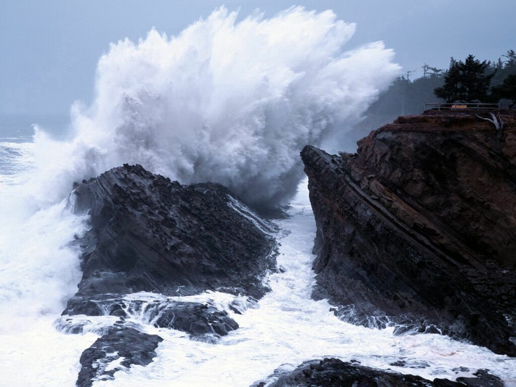 Powerful wave crashes against rugged cliffs with dramatic splashes turbulent sea in blue tones Wallpaper