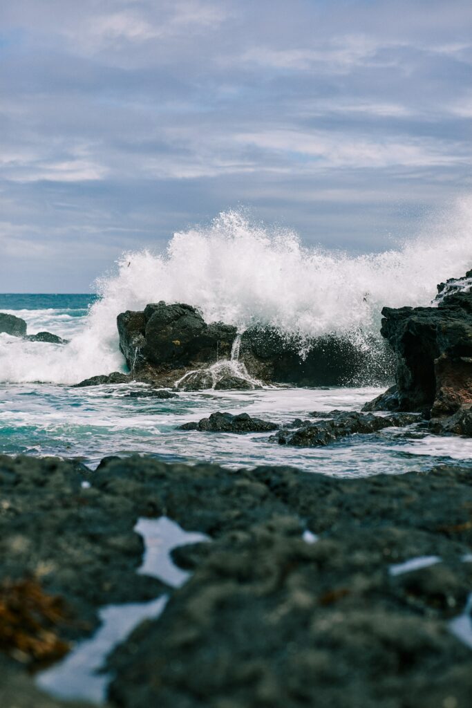 Powerful ocean wave crashing on rugged rocks under cloudy sky with sea spray and textured water Wallpaper