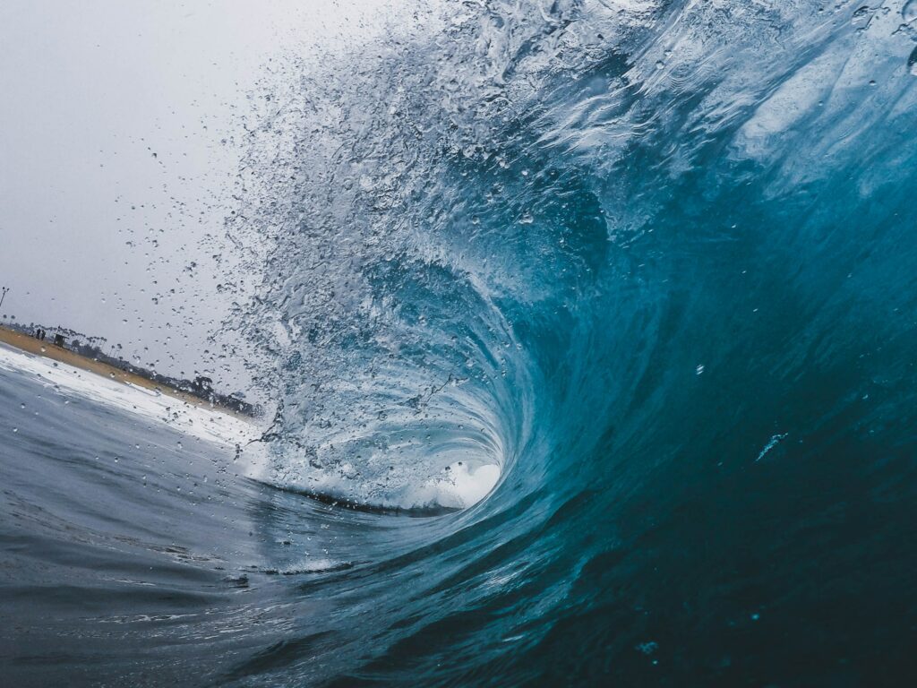 Powerful ocean wave curling to shore with vibrant blue hues and detailed water spray wallpaper