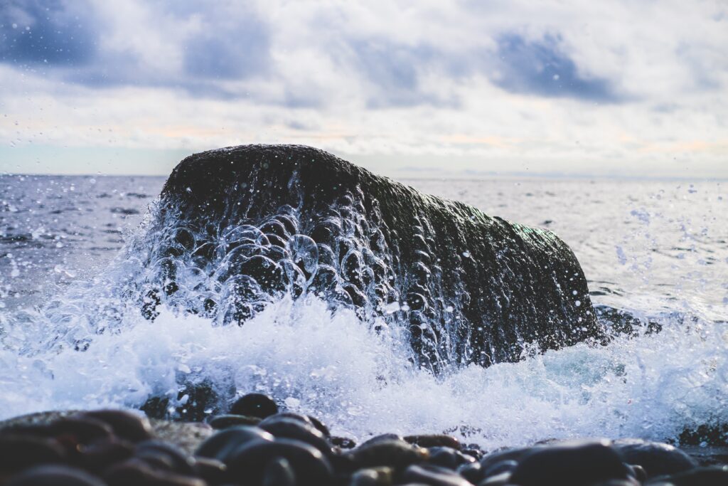 Powerful ocean waves crashing on dark rocks under dramatic cloudy sky coastal wallpaper background