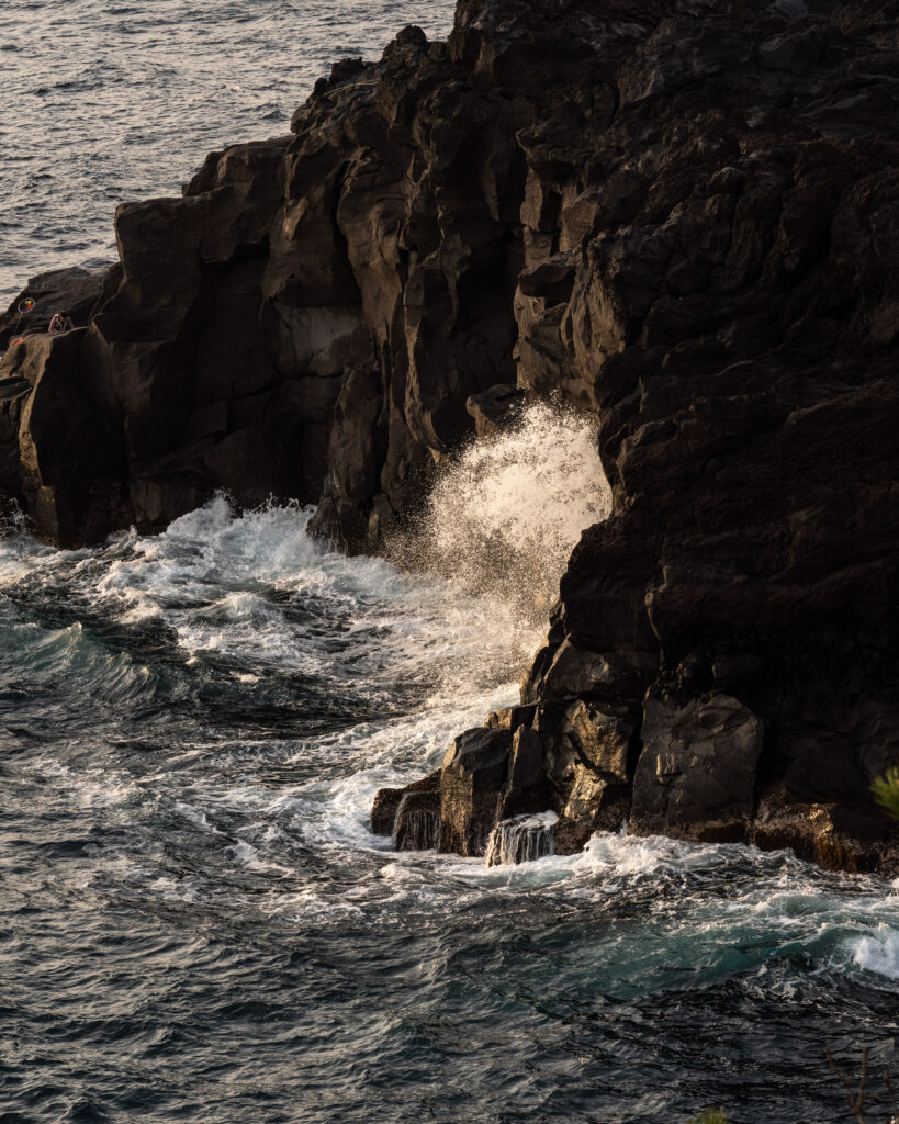 Powerful waves crash against dark rocky cliffs with dramatic spray under warm sunlight wallpaper