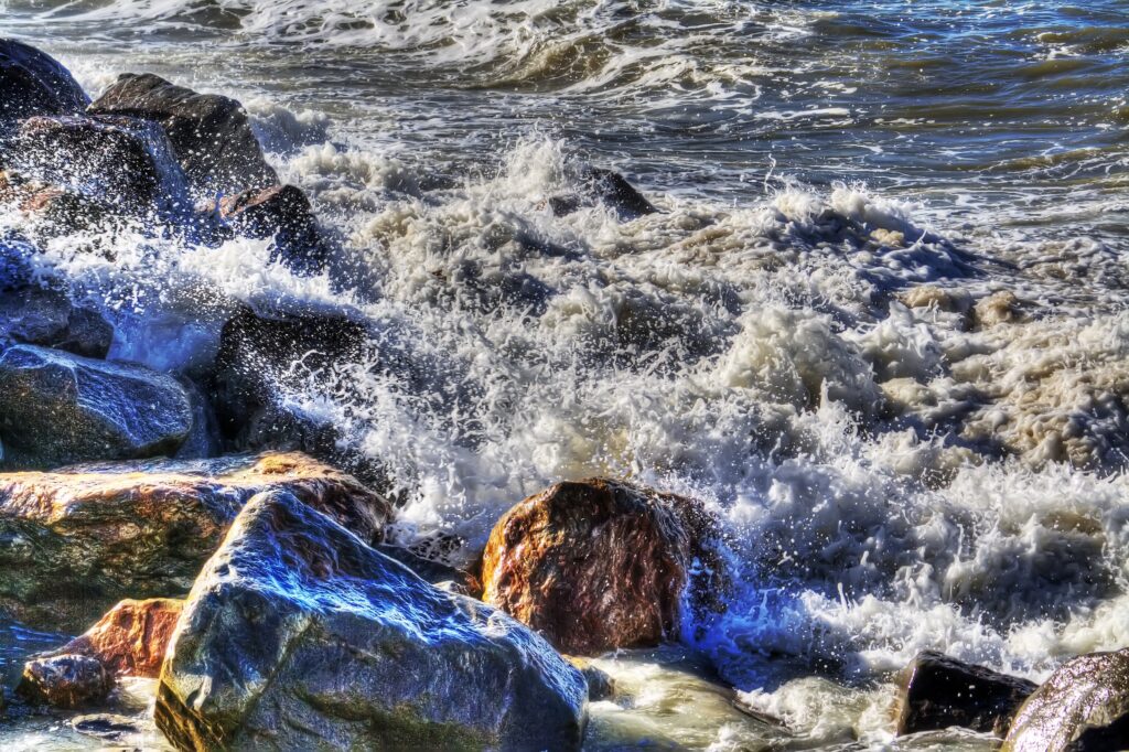 Powerful ocean waves crashing on rugged rocks with blue water and white sea foam wallpaper background