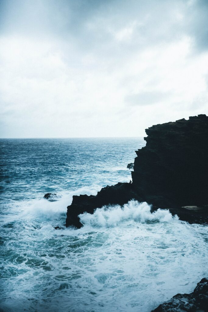Powerful ocean waves crash on rugged sea rocks under overcast sky with dynamic water spray Wallpaper