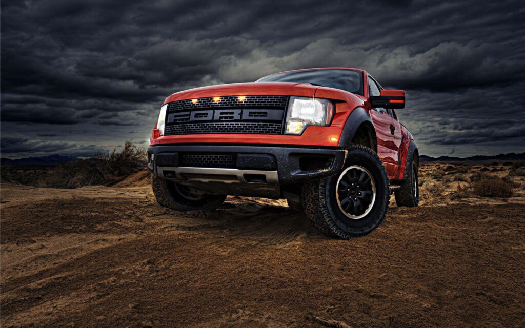 Red Ford truck on rugged dirt terrain under stormy sky showcasing off-road power wallpaper