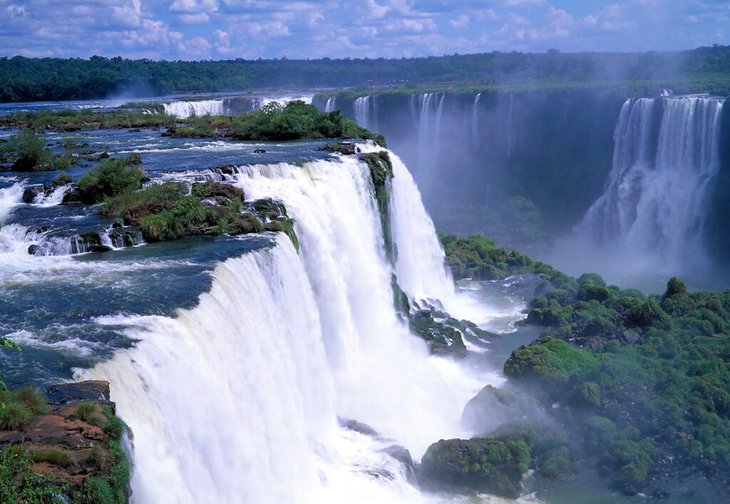 Powerful waterfall cascading over rugged rocks surrounded by lush green trees and mist Wallpaper