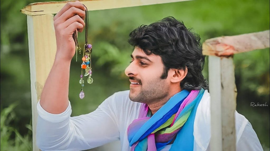 Prabhas in Darling movie wallpaper wearing white shirt and scarf admiring charm bracelet