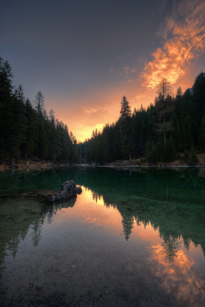 Serene Pragser Wildsee Italy sunset with emerald lake reflecting pine trees and orange clouds Wallpaper