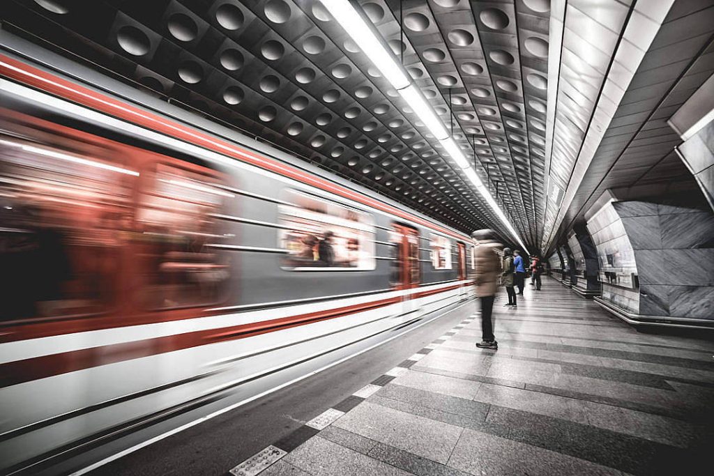 Motion-blurred train speeding through Prague Metro with commuters and dimpled metal ceiling Wallpaper