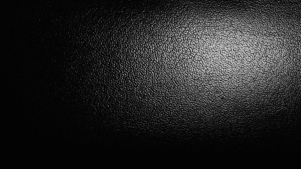 Premium black leather wallpaper macro textured grainy surface with dramatic light gradient background