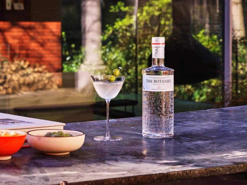 The Botanist Islay Dry Gin bottle with martini and olives on rustic wooden table background Wallpaper