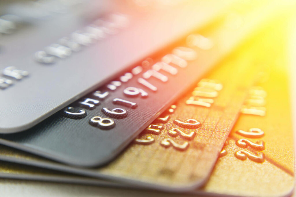 Close-up of stacked metallic credit cards in silver gold and bronze with embossed numbers and sunlight Wallpaper