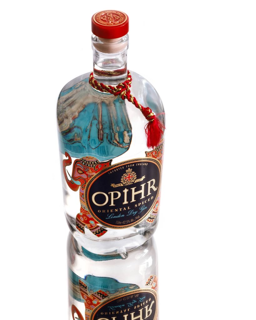 Opihr Oriental Spiced London Dry Gin bottle with vibrant elephant design and red tassel on white Wallpaper