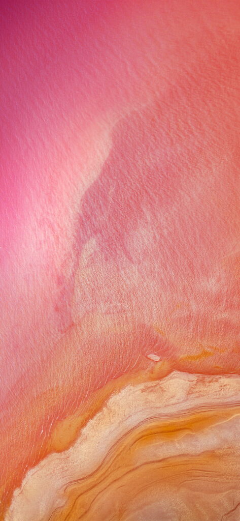 Aerial view of vibrant pink salt lake with warm orange and sandy organic textures wallpaper