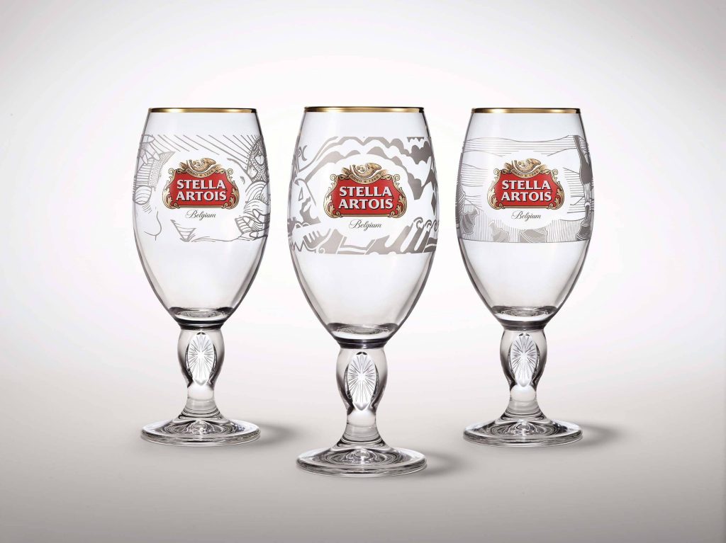 Three Stella Artois chalice glasses with gold rims and branding on minimalist light background wallpaper