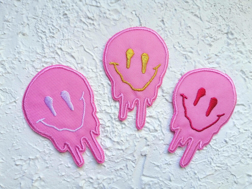 Dripping Delight: A Vibrant Trio of Pink Preppy Smiley Face Patches Adorning a Rough White Background Wallpaper