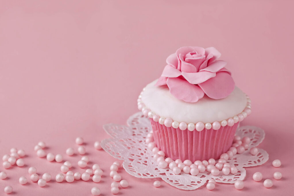Elegant white frosted cupcake with pink fondant rose and pearls on lace doily background Wallpaper