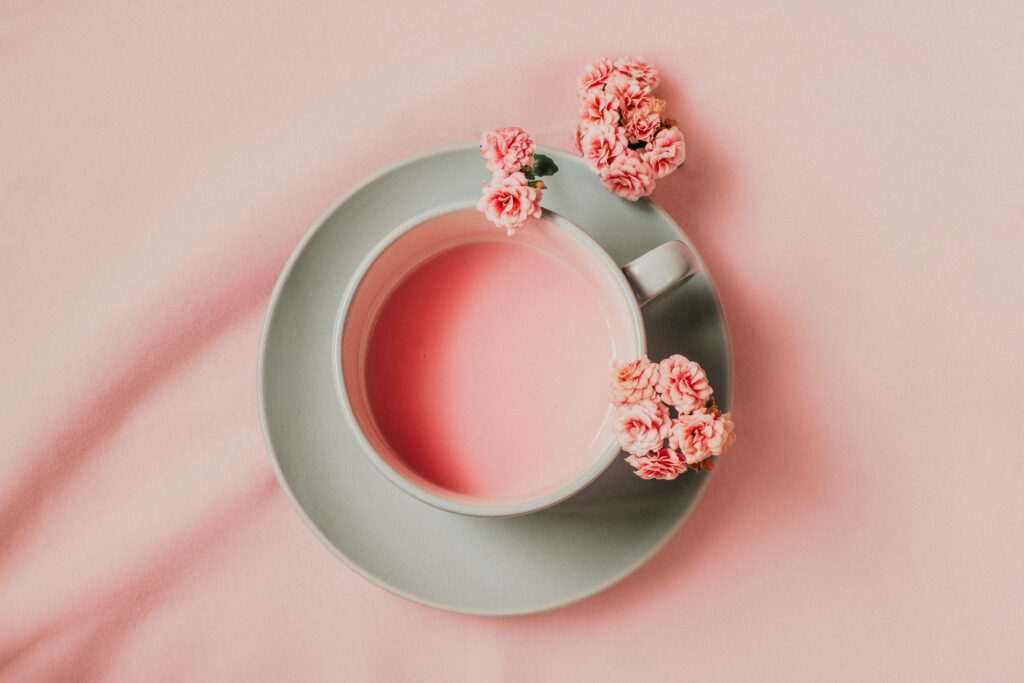 Minimalist soft grey teacup with creamy pink liquid and pink blossoms on pastel background wallpaper