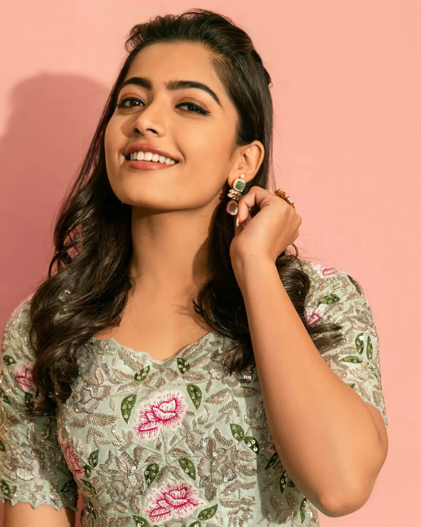 Radiant Rashmika Mandanna Dazzling in a Vibrant Green Floral Blouse Against a Blush Pink Backdrop – HD Image Wallpaper