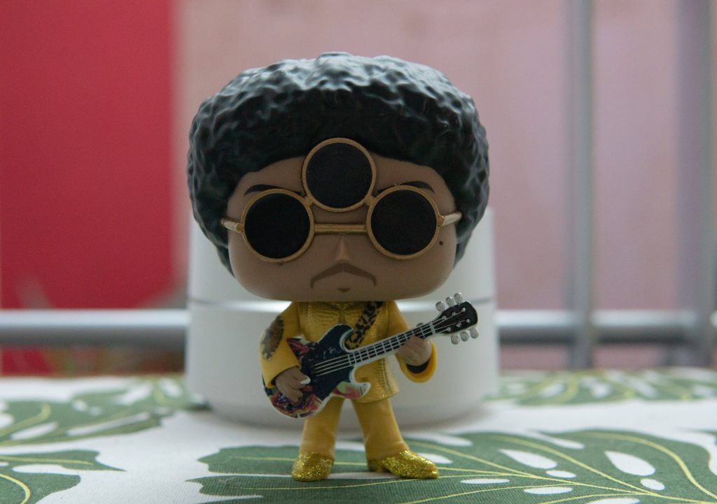 Close-up Funko Pop of Prince in yellow 3rd Eye Girl suit with guitar vibrant wallpaper background