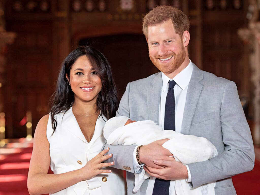 Prince Harry and Meghan Markle smiling holding newborn son Archie wrapped in white blanket indoors Wallpaper