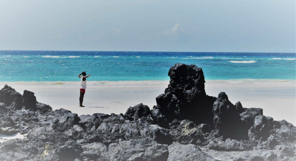 Scenic Comoros Island: Person Gazes at Turquoise Waves & Volcanic Rocks Wallpaper