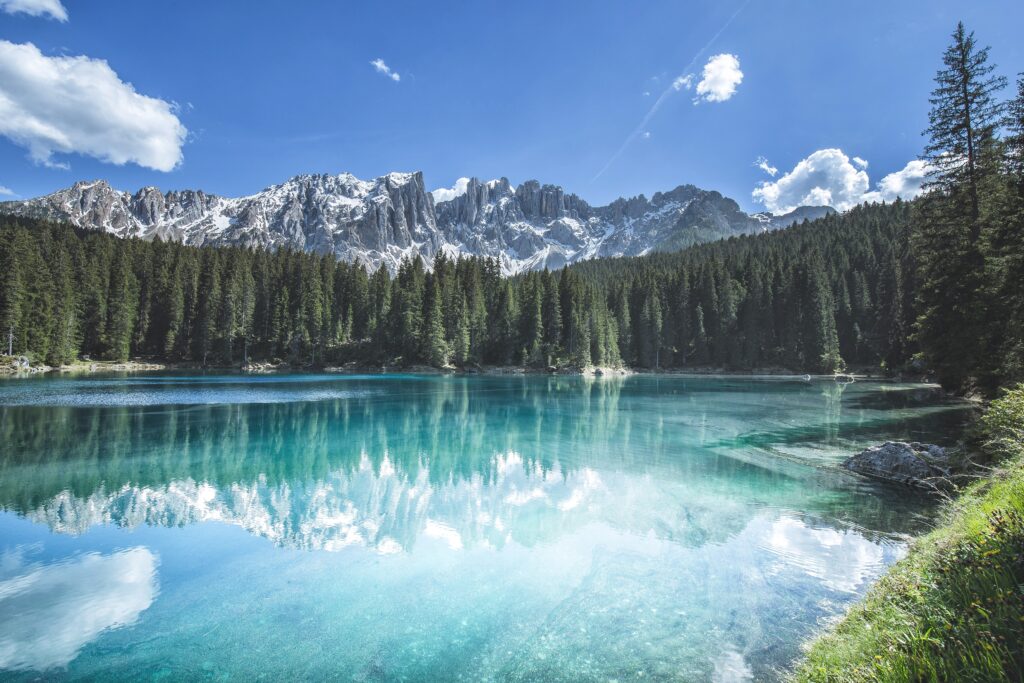Crystal-clear lake reflecting evergreen forest and snow-capped mountains under blue sky wallpaper