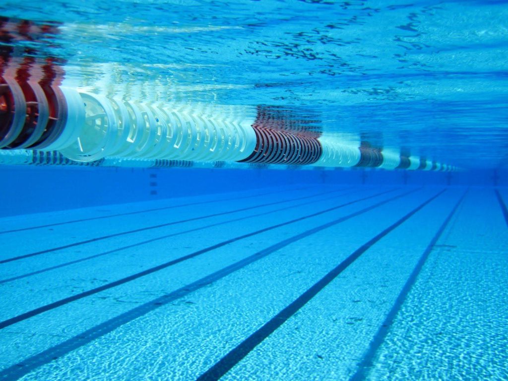 Underwater view of a clean swimming pool with red and white lane rope and sunlight patterns Wallpaper