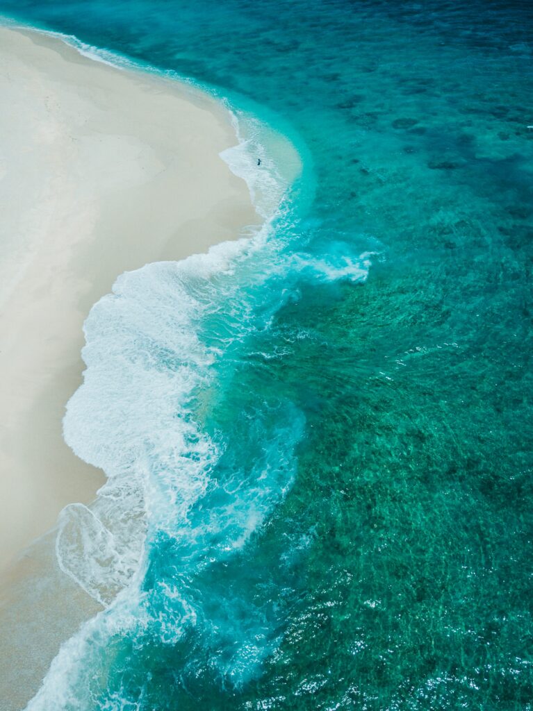 Aerial view of turquoise waves gently meeting soft sandy beach showcasing tranquil shoreline Wallpaper