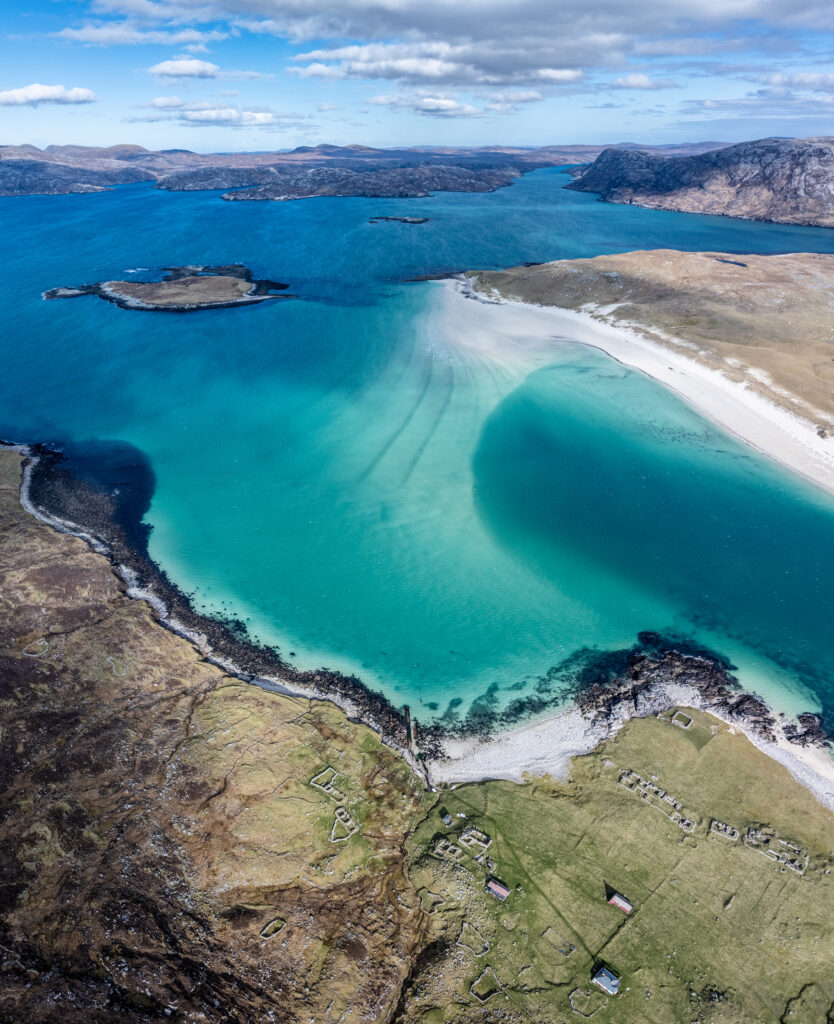 Aerial view of turquoise sea meeting sandy shore with rugged terrain and scattered islands Wallpaper