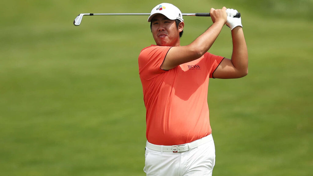 Pro golfer An Byeong-hun mid-swing on green course wearing orange shirt and white cap golf wallpaper