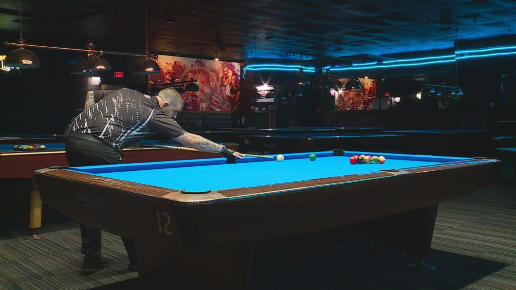 Professional billiards player aiming precise shot on vibrant blue pool table in stylish hall Wallpaper