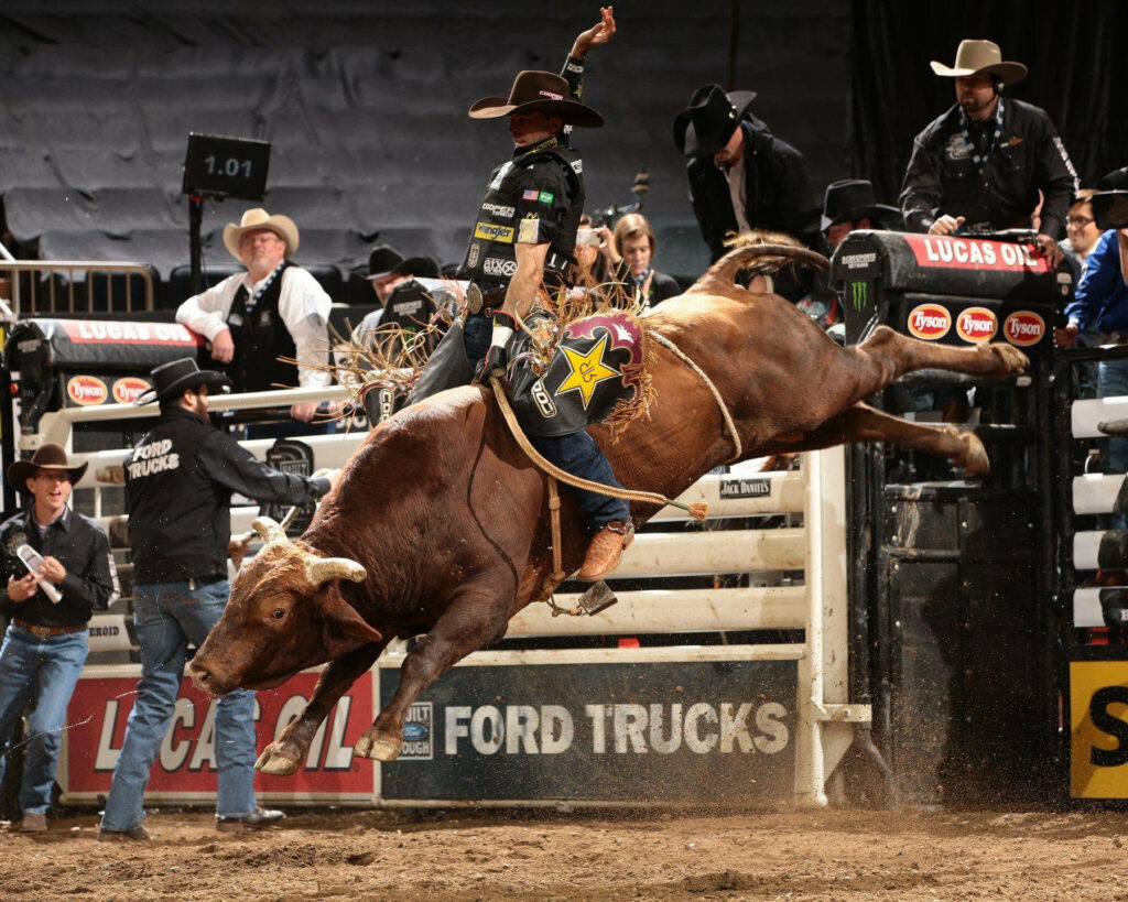 Professional bull rider mid-ride in dynamic arena with earthy tones and dramatic lighting wallpaper