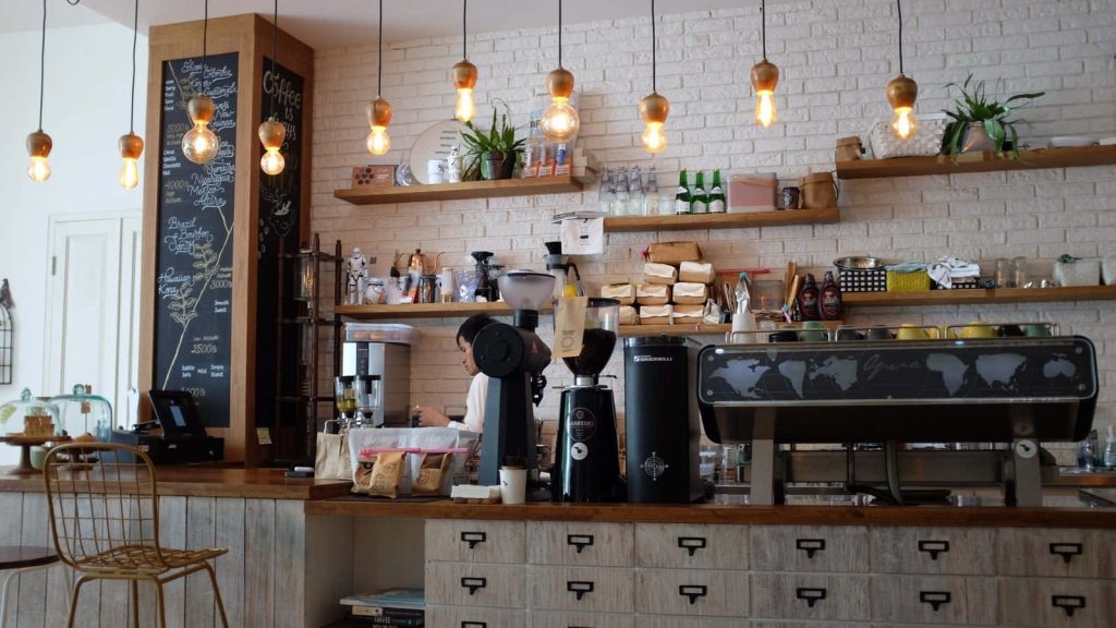 Modern coffee shop Zoom background with warm Edison bulbs white brick walls and espresso machine Wallpaper