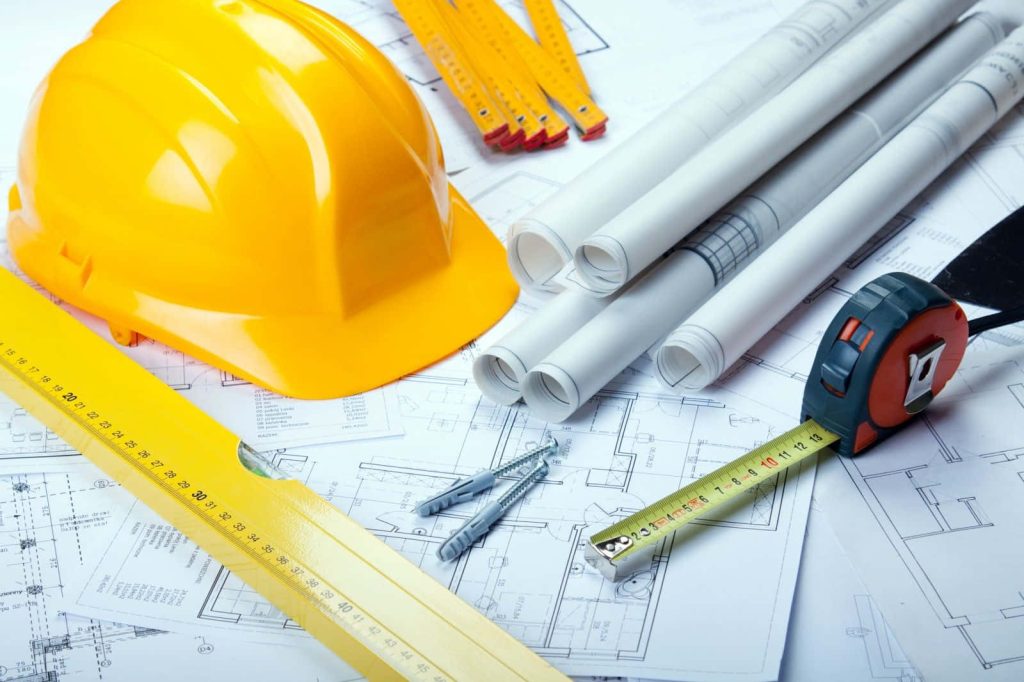 Yellow hard hat with architectural blueprints wooden ruler and tape measure on construction site background Wallpaper