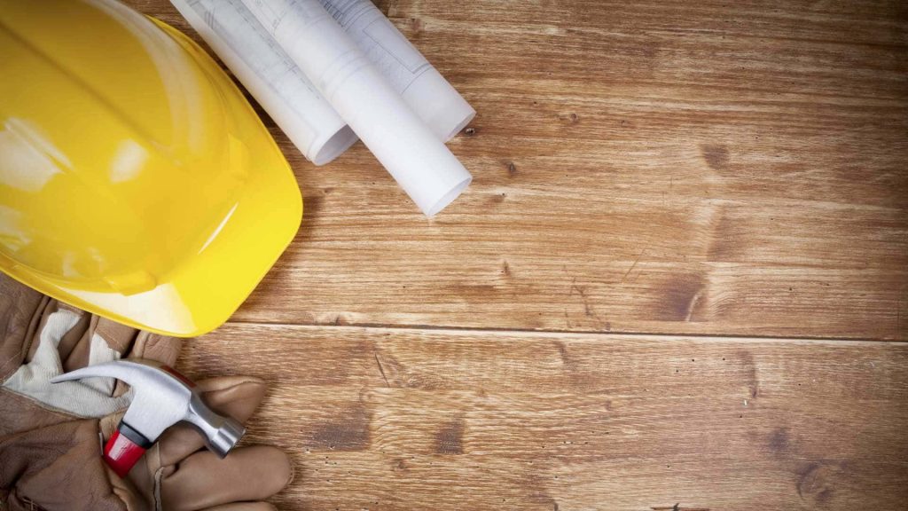 Yellow hard hat blueprints gloves and hammer on rustic wood construction workspace background Wallpaper