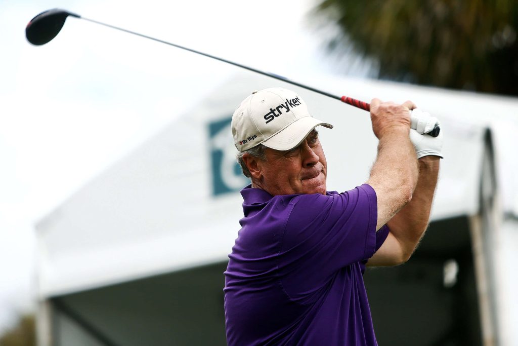Professional golfer Hal Sutton mid-swing in purple polo and beige Stryker cap at tournament Wallpaper