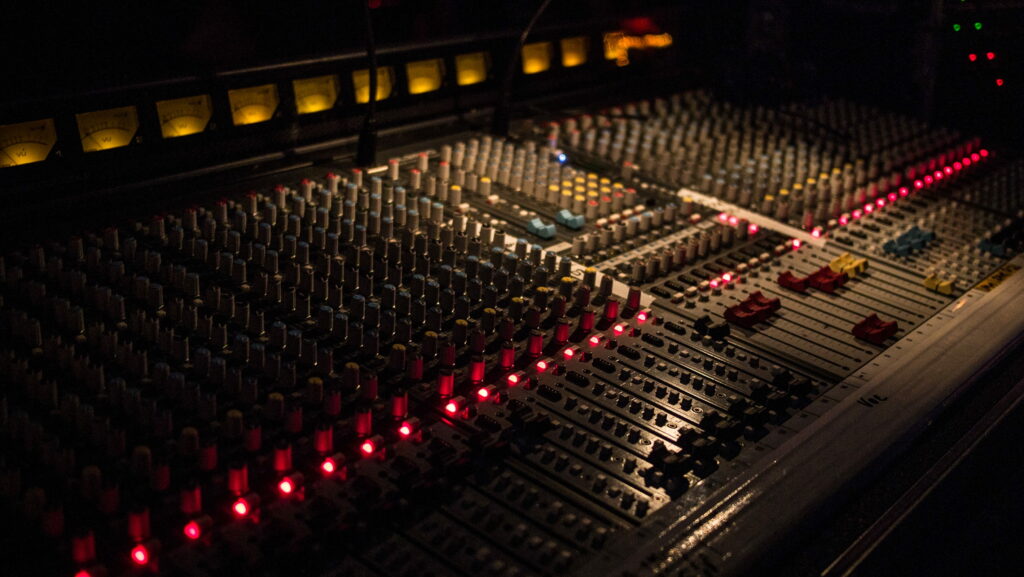 Professional audio mixing console with red LED faders and amber VU meters on studio desk Wallpaper