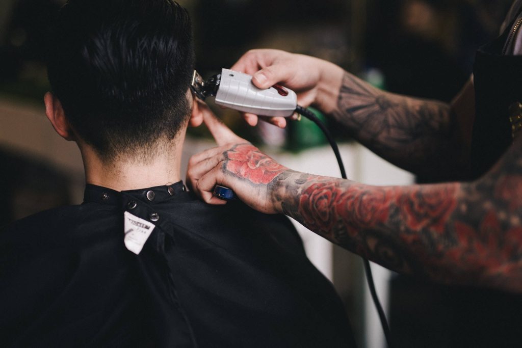 Tattooed barber expertly shaving sides of man’s hair with clippers detailed floral ink haircut Wallpaper