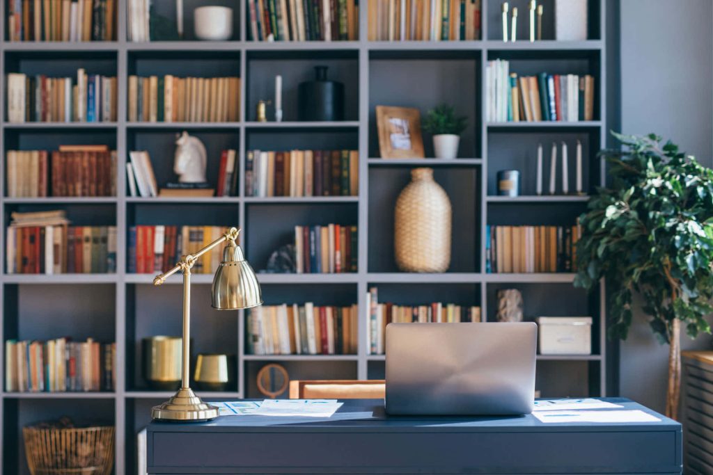 Professional virtual office Zoom background with desk laptop brass lamp and dark bookshelf Wallpaper
