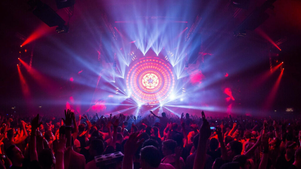 Vibrant live music festival with glowing circular stage and cheering crowd in purple red light Wallpaper